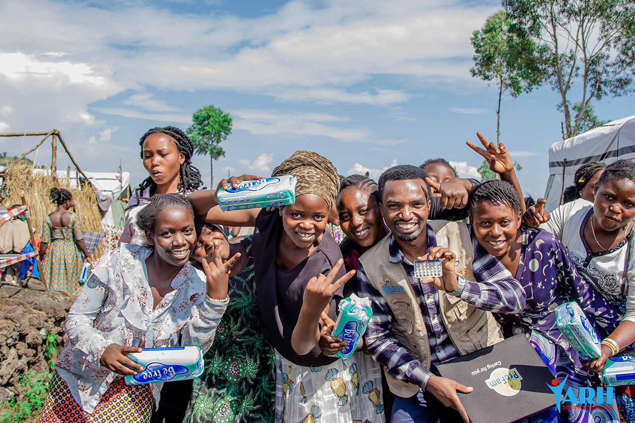 Dr. Simon Bine Mambo (shown center) and camp residents pose with contraception and menstrual hygiene supplies available at the clinic.