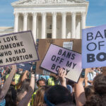 A crowd of people holding signs at a protest. The signs include messages like "Pro-Science Pro-Choice," "I Love Someone Who Had An Abortion," "Bans Off My Body," and "Bans Off Our Bodies." The U.S. Supreme Court building is visible in the background.