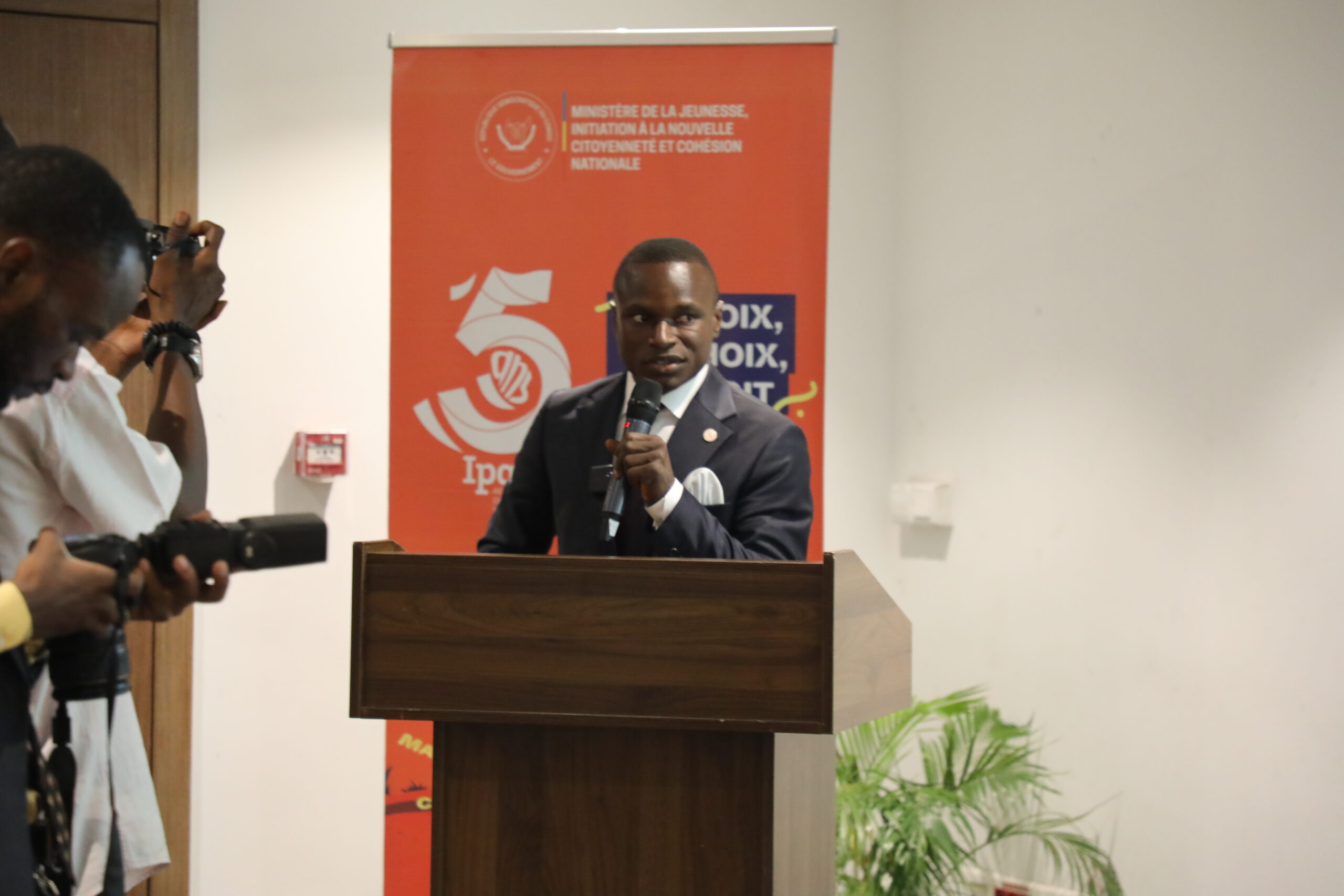 A man in a suit delivering a speech at a podium, addressing an audience with confidence and authority.