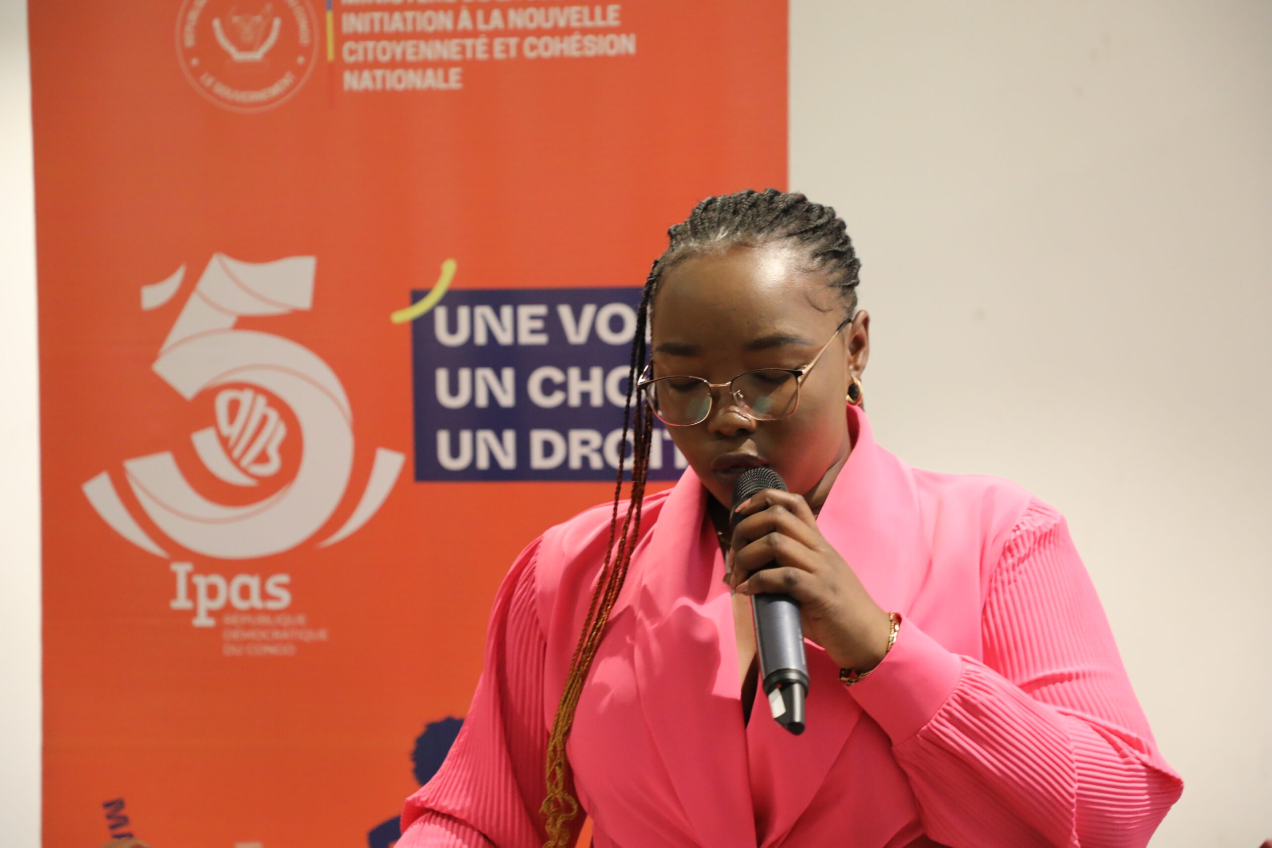 A woman in a pink shirt speaking with conviction into a microphone at an event.