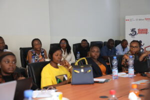 a group of people sitting at long classroom-style tables and watching and listening to a presenter