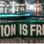 Large green banner set in front of a backdrop of Washington DC at night that reads "Abortion is freedom"