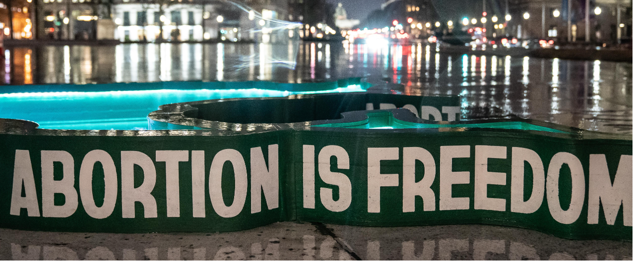 Large green banner set in front of a backdrop of Washington DC at night that reads "Abortion is freedom"
