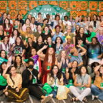 A large group of people posing for a photo at a Green Wave gathering, many holding small green flags that say “Abortion Freedom.”