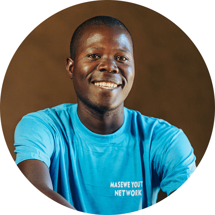 A smiling man wearing a bright blue "Masewe Youth Network" T-shirt sits in front of a plain brown background.