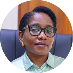A woman with short hair wearing glasses, yellow earrings, and a light green collared shirt sits in a dark office chair with a wooden background behind her.