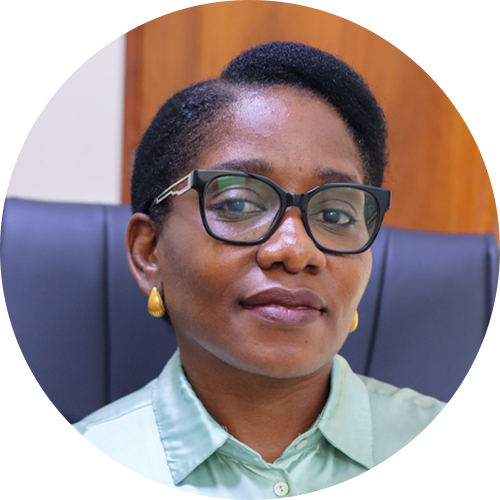 A woman with short hair wearing glasses, yellow earrings, and a light green collared shirt sits in a dark office chair with a wooden background behind her.