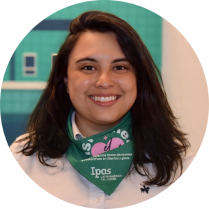 A person with long dark hair smiles at the camera, wearing a white shirt and a green bandana with text and logos around their neck. The background is teal with some blurred shapes.