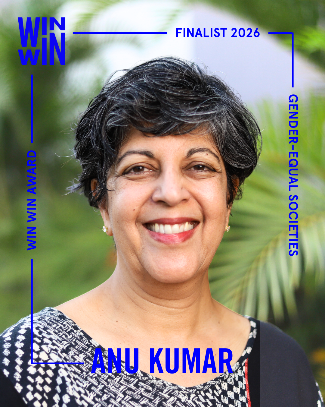 A woman with short, curly gray hair smiles at the camera. Text around her reads “WIN WIN AWARD,” “FINALIST 2026,” “GENDER-EQUAL SOCIETIES,” and “ANU KUMAR.” Green leaves are blurred in the background.