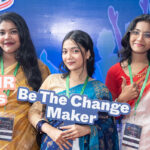 Three women in traditional attire hold colorful signs reading “We are SRHR Champions,” “Be The Change Maker,” and “SRHR: Because We Care” at a youth event with a blue backdrop.