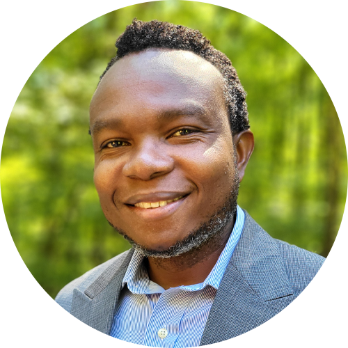 Portrait of Dr. Mike Mpoyi, a smiling man with short curly hair and a trimmed beard, wearing a gray blazer and blue striped shirt, standing outdoors with a blurred green background—a dedicated advocate for reproductive health in the DRC with experience supporting Ipas initiatives during the Ebola response.